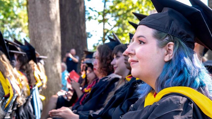 2023年8月毕业典礼上，毕业生们坐在森林树林校园的橡树下.
