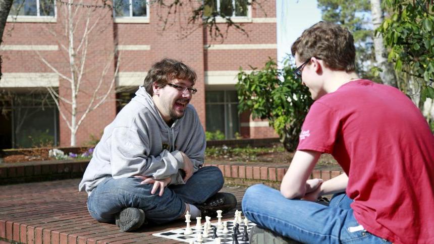 Two male students playing chess on a brick ledge