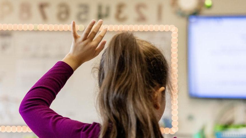 An elementary school student raises their hand in a classroom.